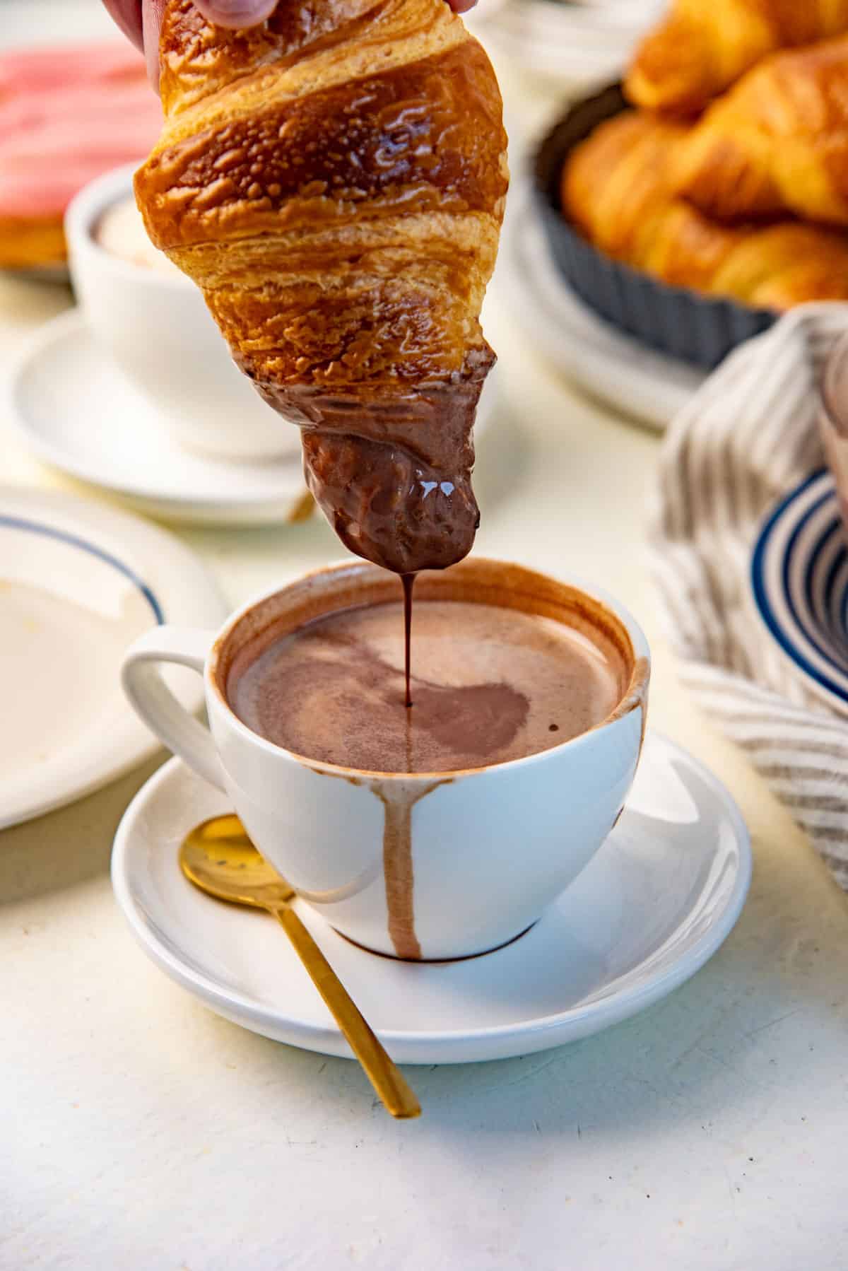 A close up of a flaky croissant being dipped in the Parisian hot chocolate.
