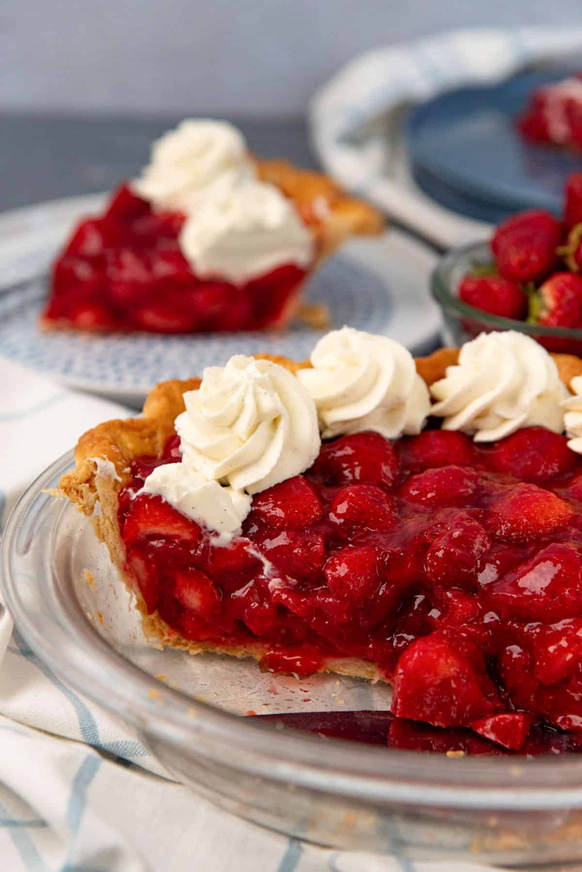 Cross section of fresh strawberry pie with whipped cream topping showing juicy strawberries in the filling.