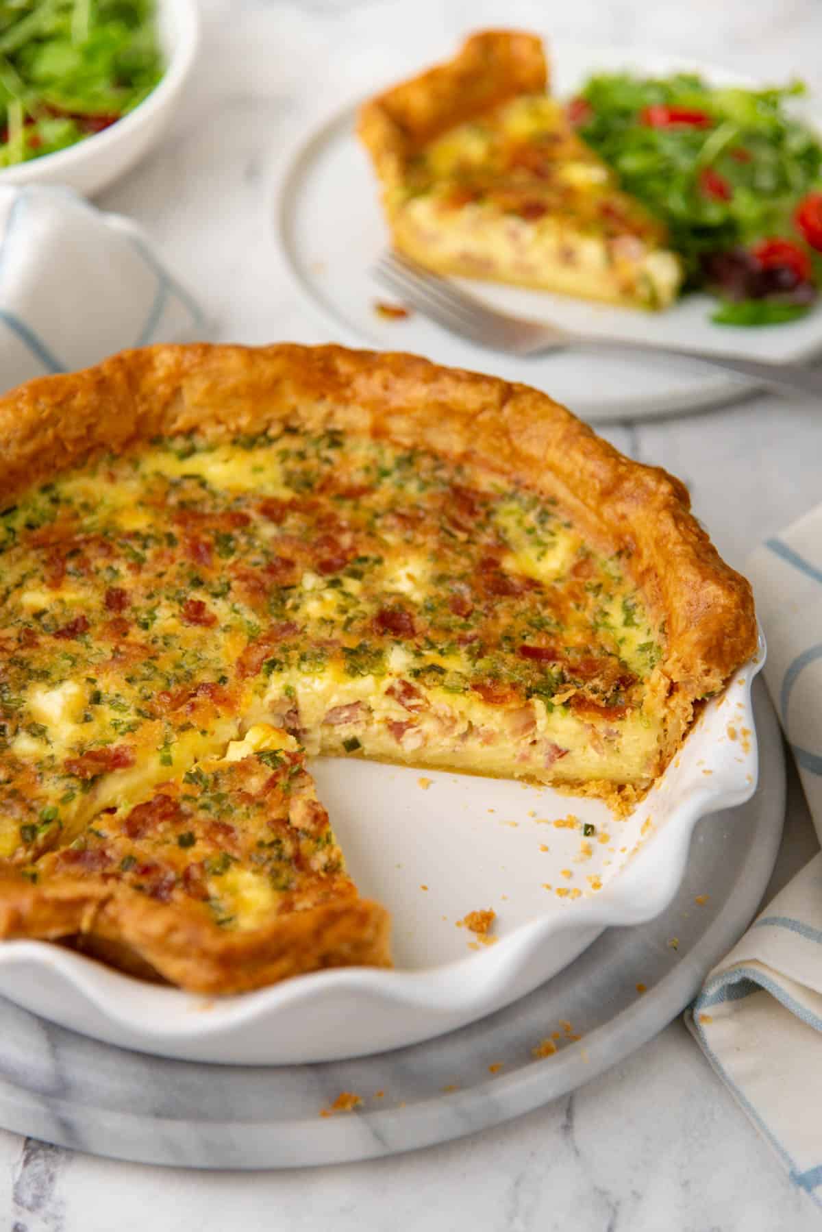 A view of quiche made with bacon, in a pie dish, with the inside of the filling visible.