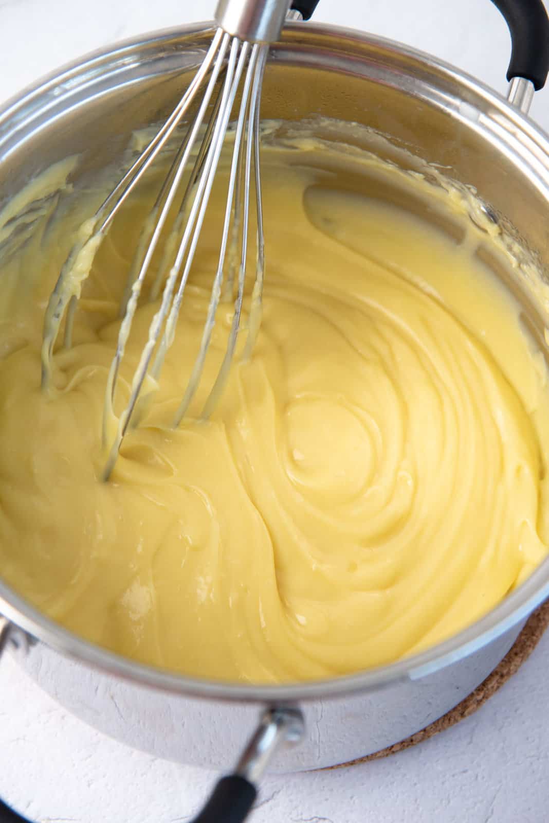 Pastry cream being whisked in a saucepan.