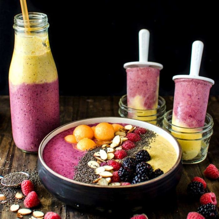 One yellow and pink mango peanut butter smoothie bowl, smoothie in a bottle, and two smoothie popsicles.