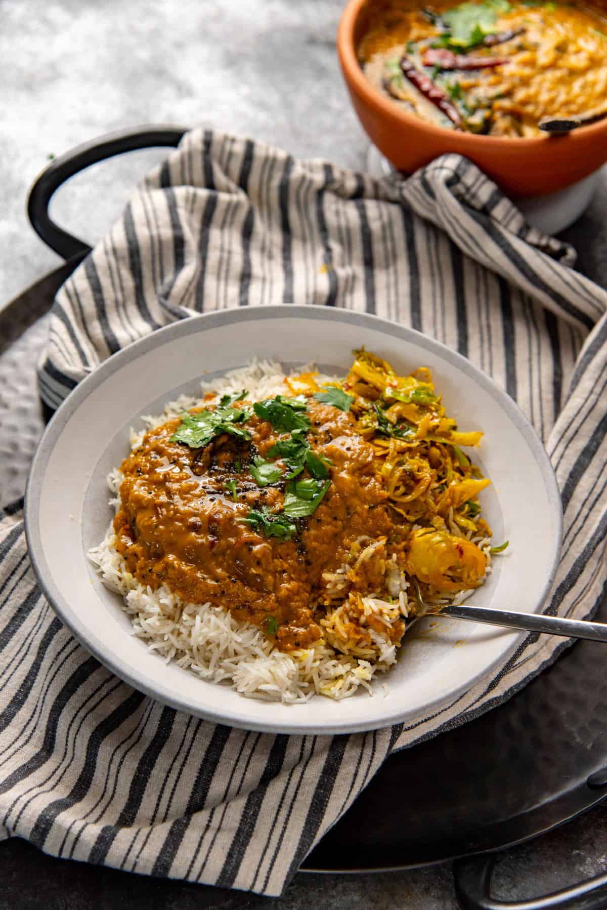 Tempered red lentil curry served over a bed of white rice and other sides in a gray plate.