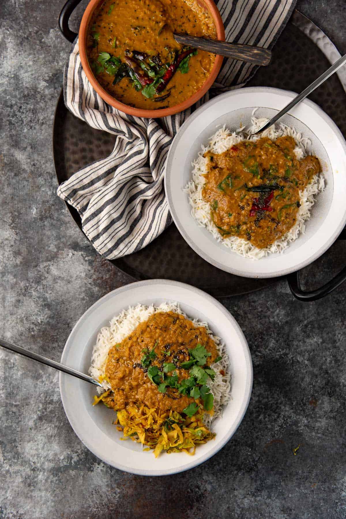 Two rice bowls topped with dhal curry, with one plain variation and a spinach and lentil curry variation.
