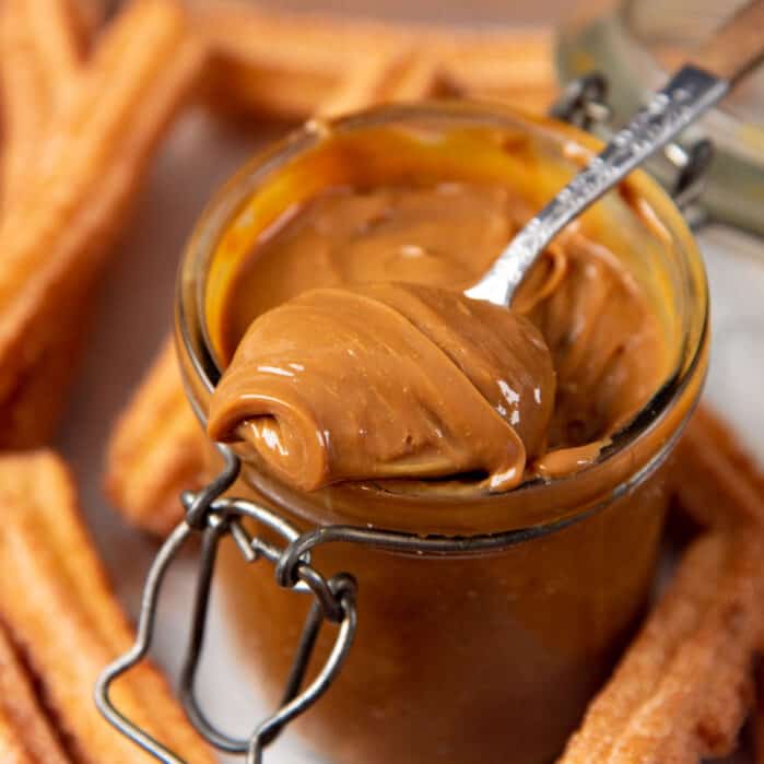 A close up of a spoonful of dulce de leche from a jar of dulce de leche.