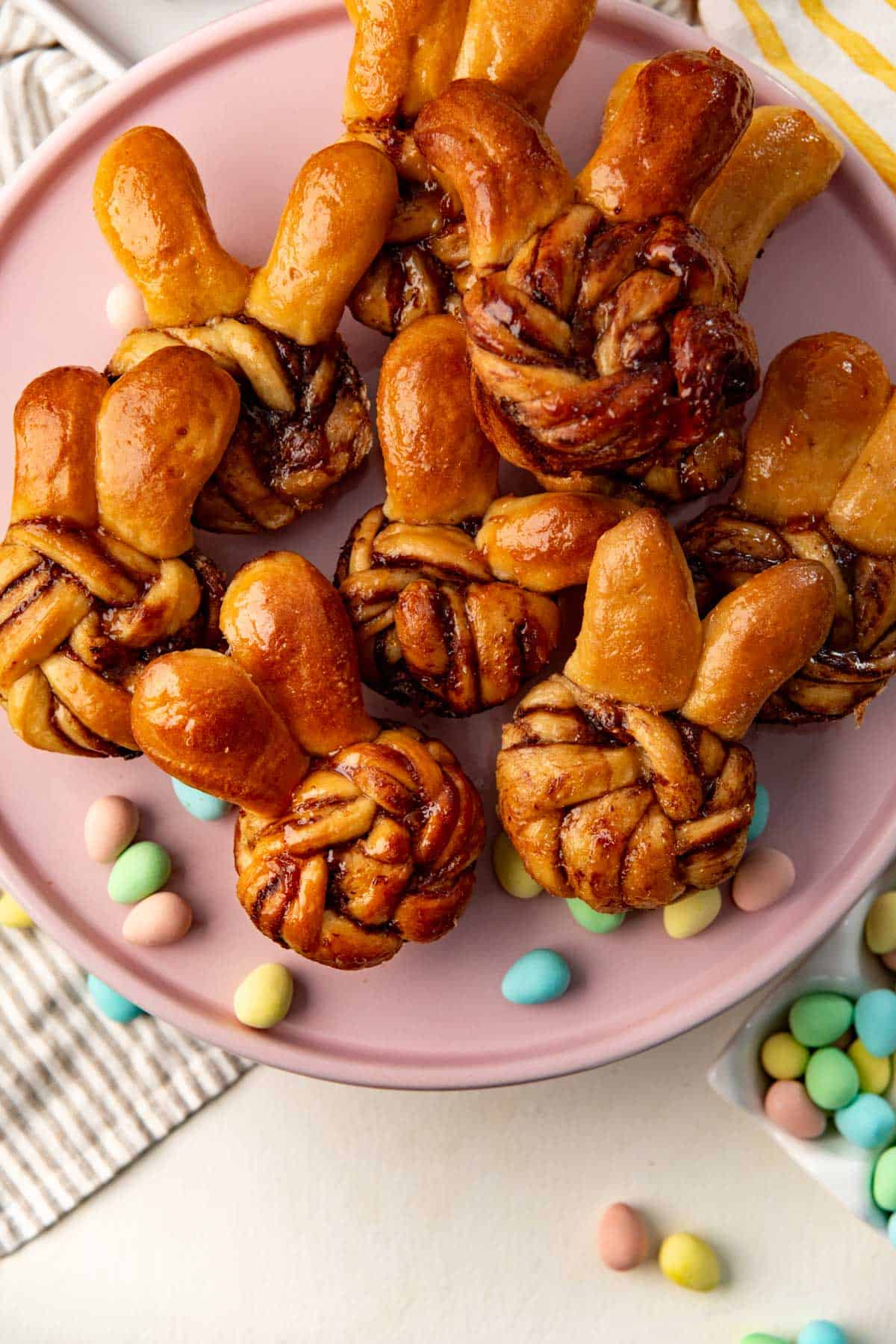 Overhead image of Easter bunny buns on a pink plate and chocolate mini eggs sprinkled around them.