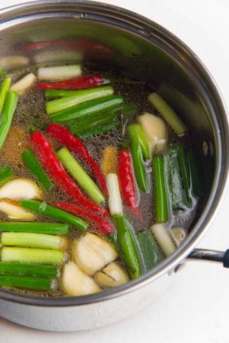 Process of making the chicken ramen broth - Chicken stock in a saucepan with garlic, ginger, spring onions and chili.