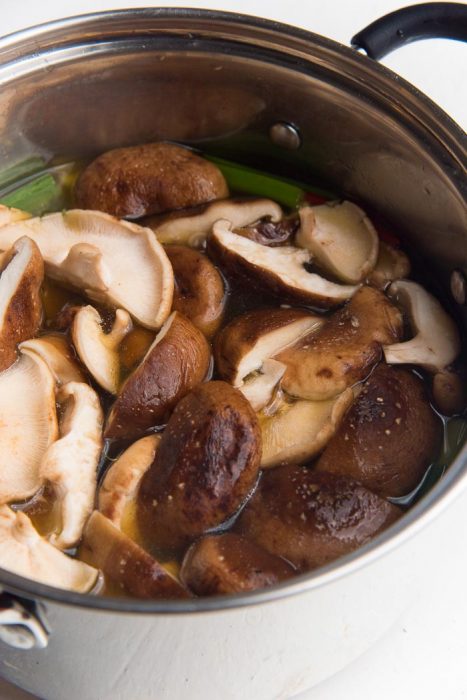 Shiitake mushrooms added to the shoyu ramen broth in a saucepan.
