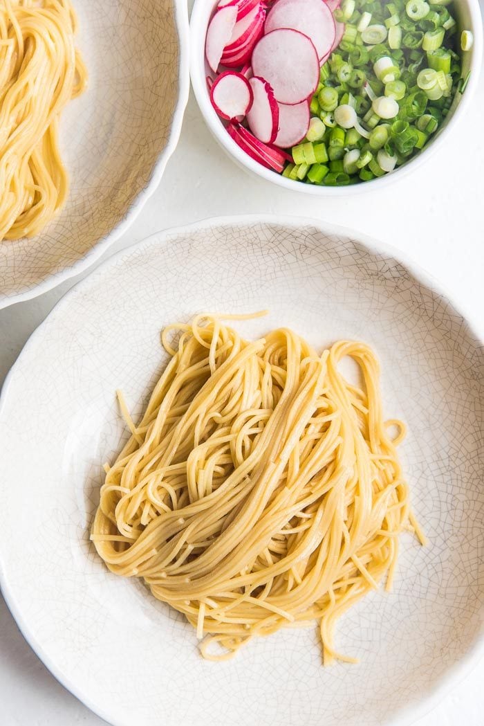 A large white bowl, with cooked straight ramen noodles added to the center of the bowl.
