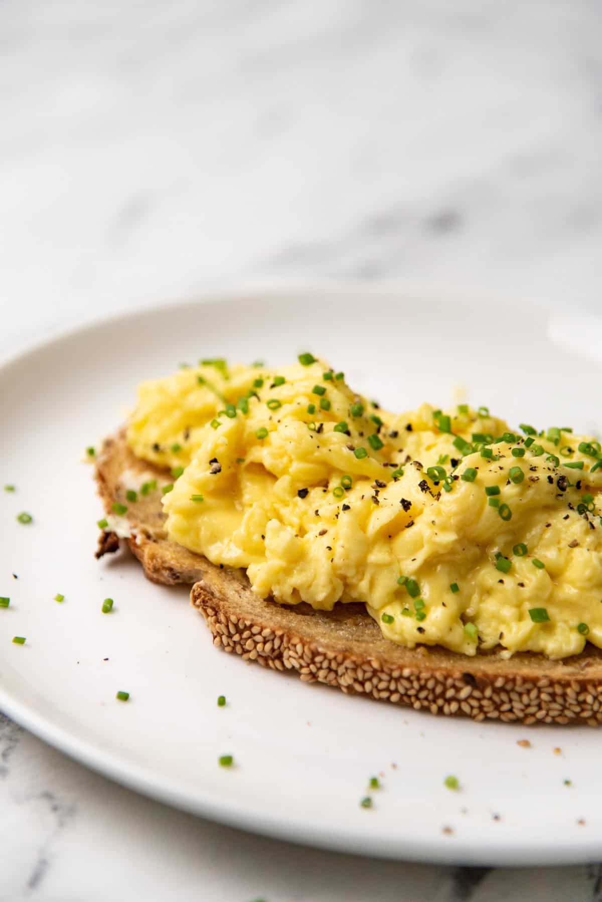 Close up of soft scrambled eggs served ontop of toast with black pepper and chives.