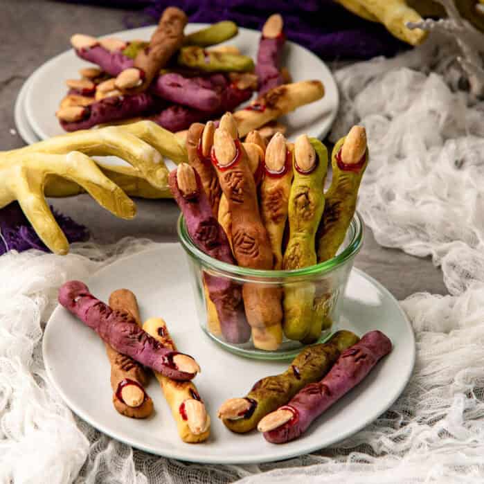 Witch finger cookies in a small glass bowl, with a witch's hand prop in the background.