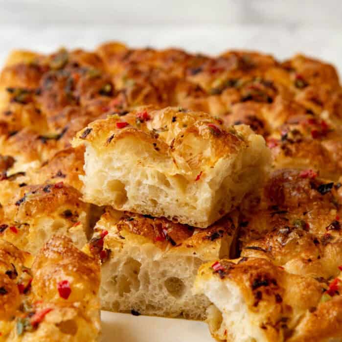 A cut piece of focaccia bread sitting on top of the rest of the bread showing the bubbly, airy crumb.