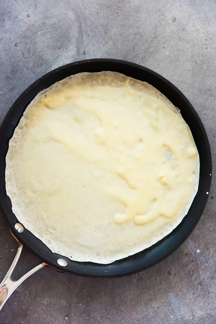 Crepe batter swirled on to a hot non stick pan. The batter has just been set, but the edges are not colored yet. 