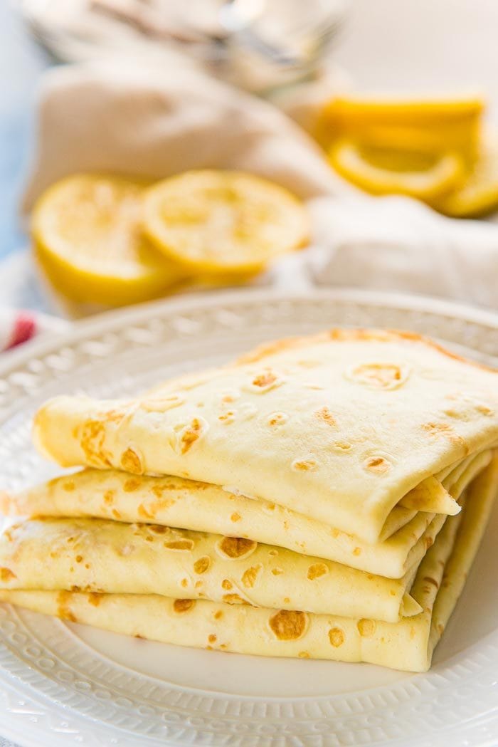 A stack of delicious crepes, folded over into quarters, on a plate. 
