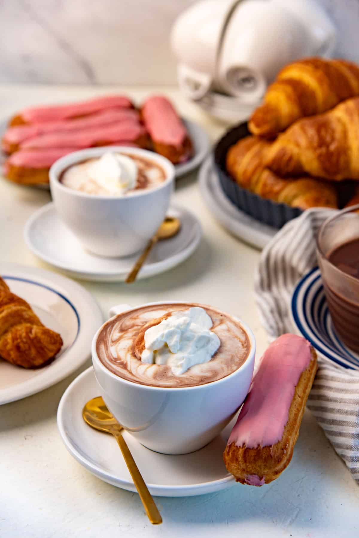 French hot chocolate served warm in small coffee cups with whipped cream and croissants.