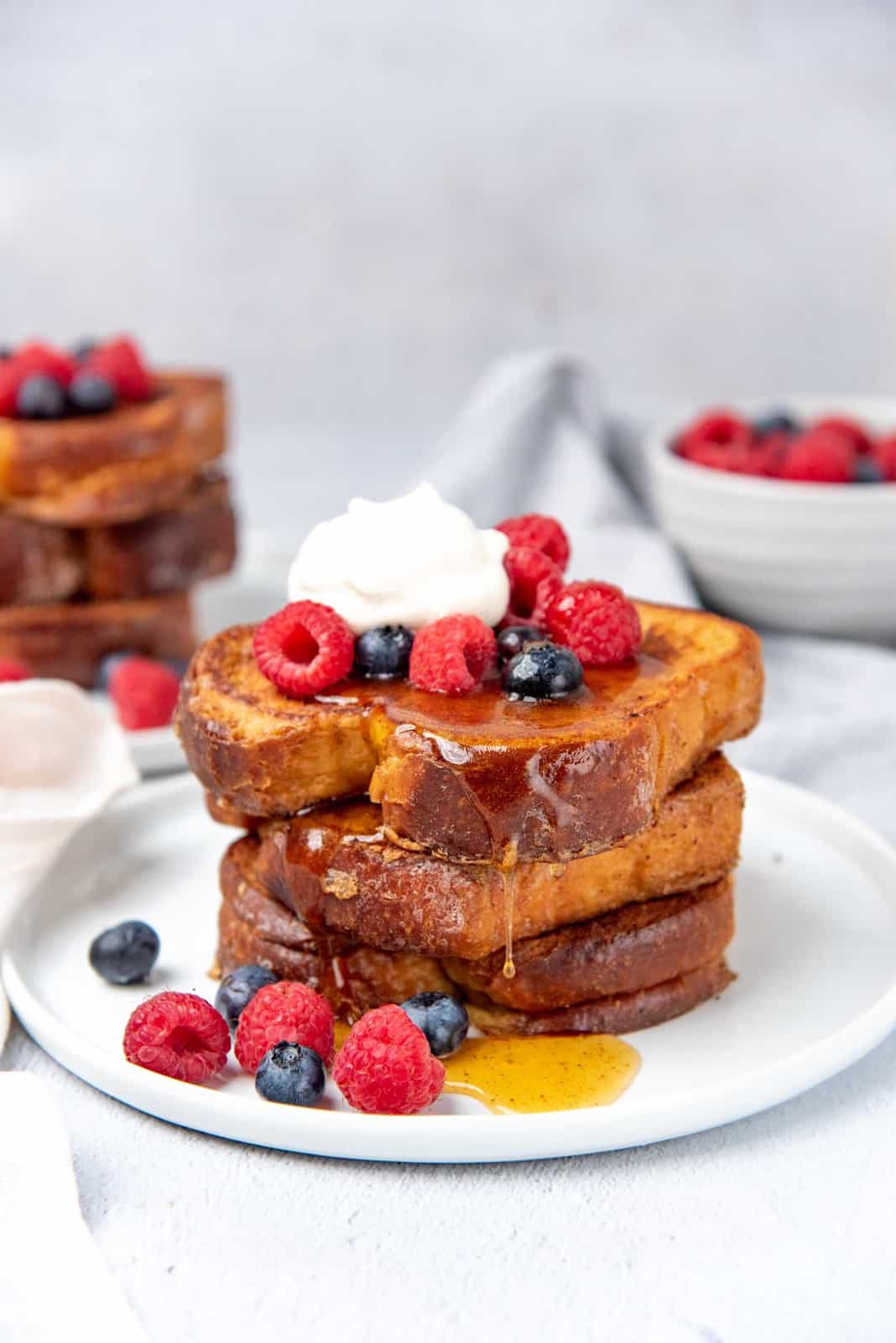 Stack of french toast on a white plate with fresh fruits and syrup