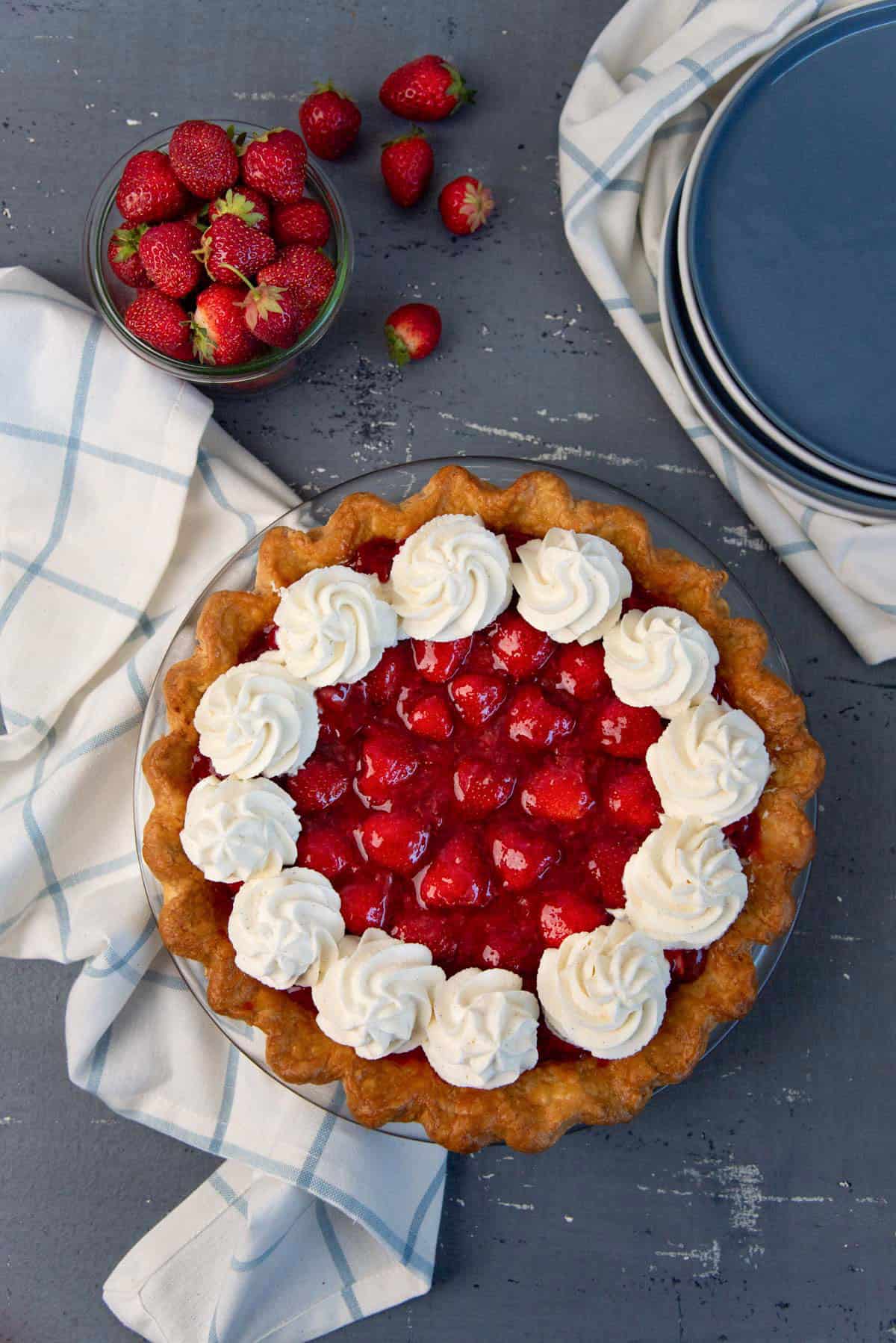 Filled strawberry pie with whipped cream swirls on top.