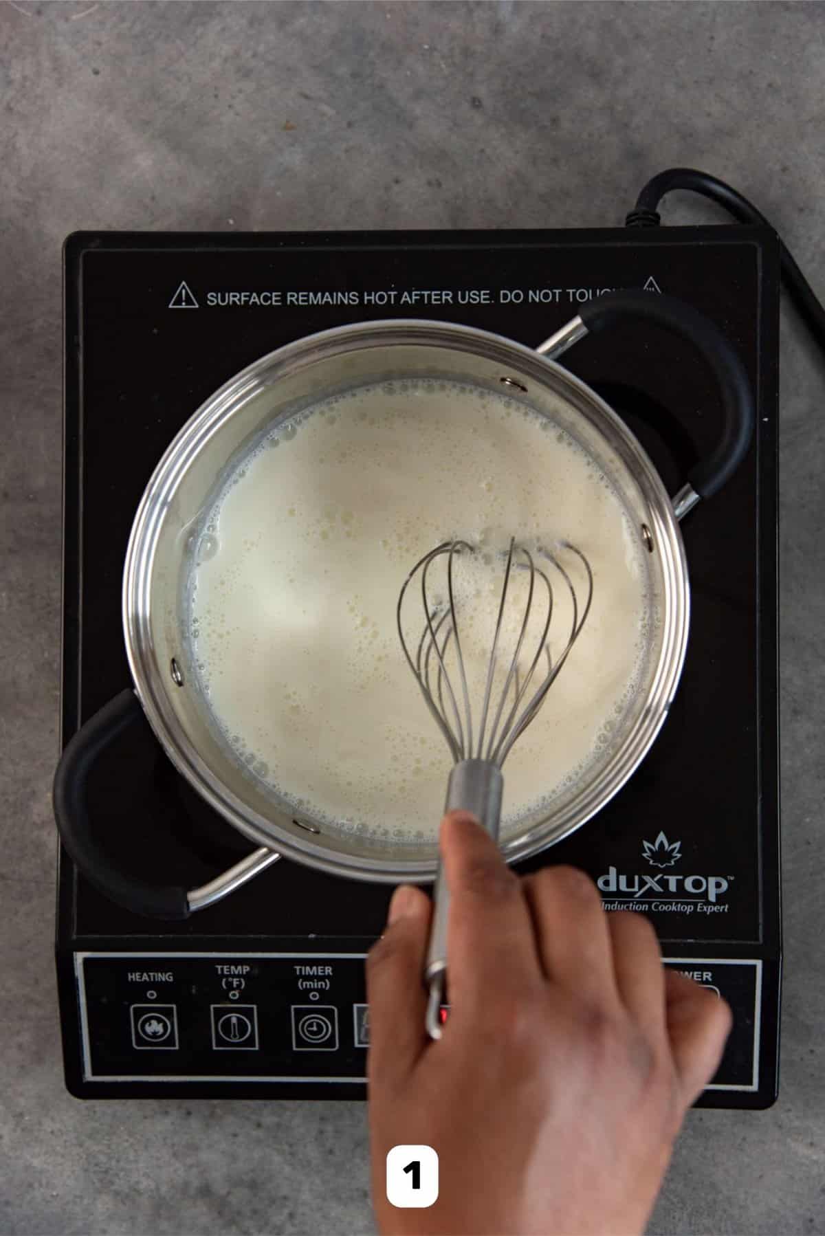 Heating the milk on the stove, using a whisk to heat the milk evenly.
