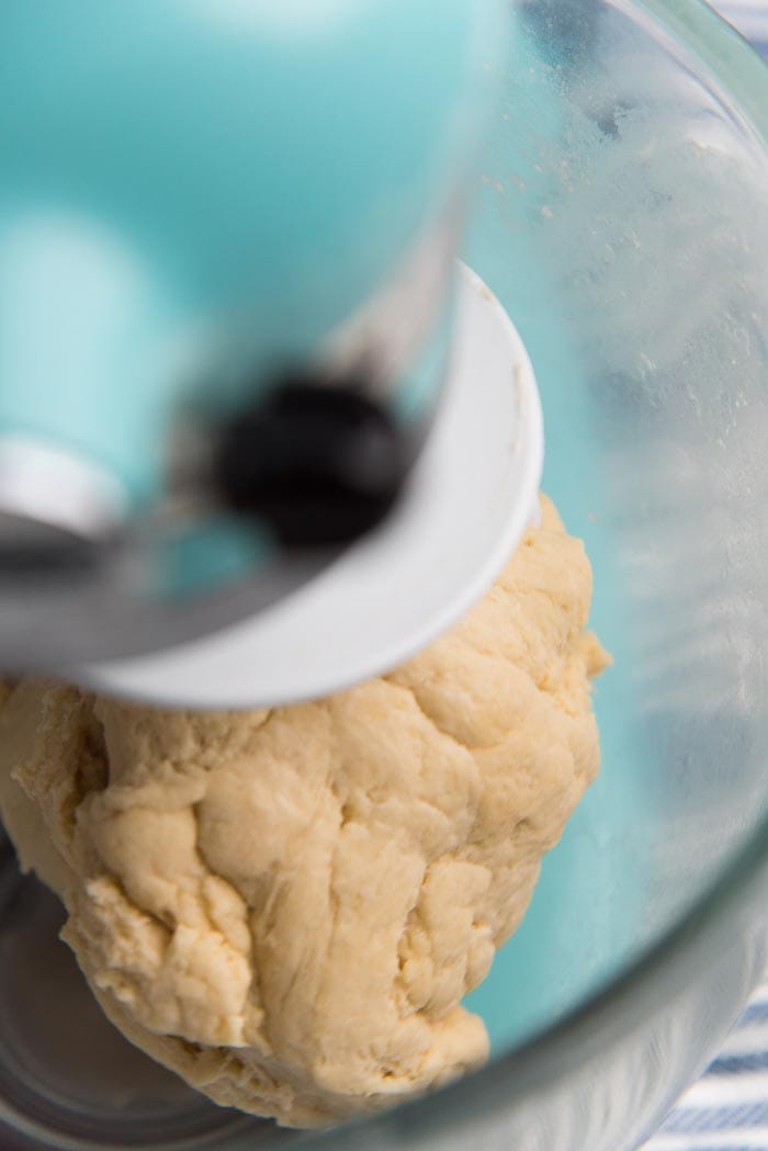 Bread dough being kneaded in mixer bowl.
