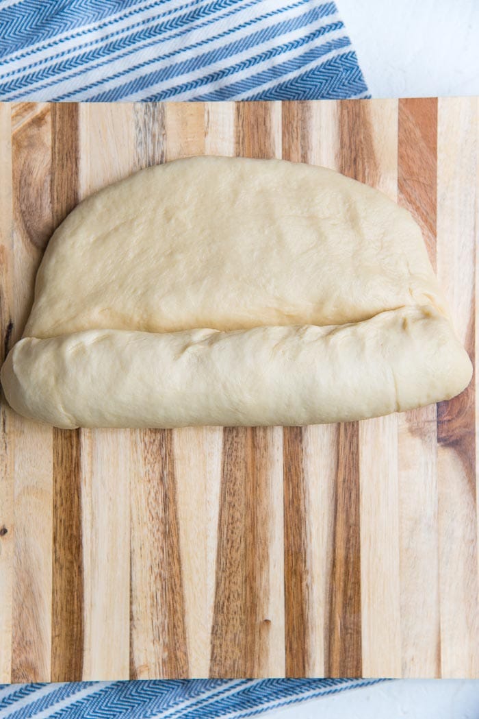 Rolling up the dough more while pressing the dough into itself to make sure it's tightly wrapped.