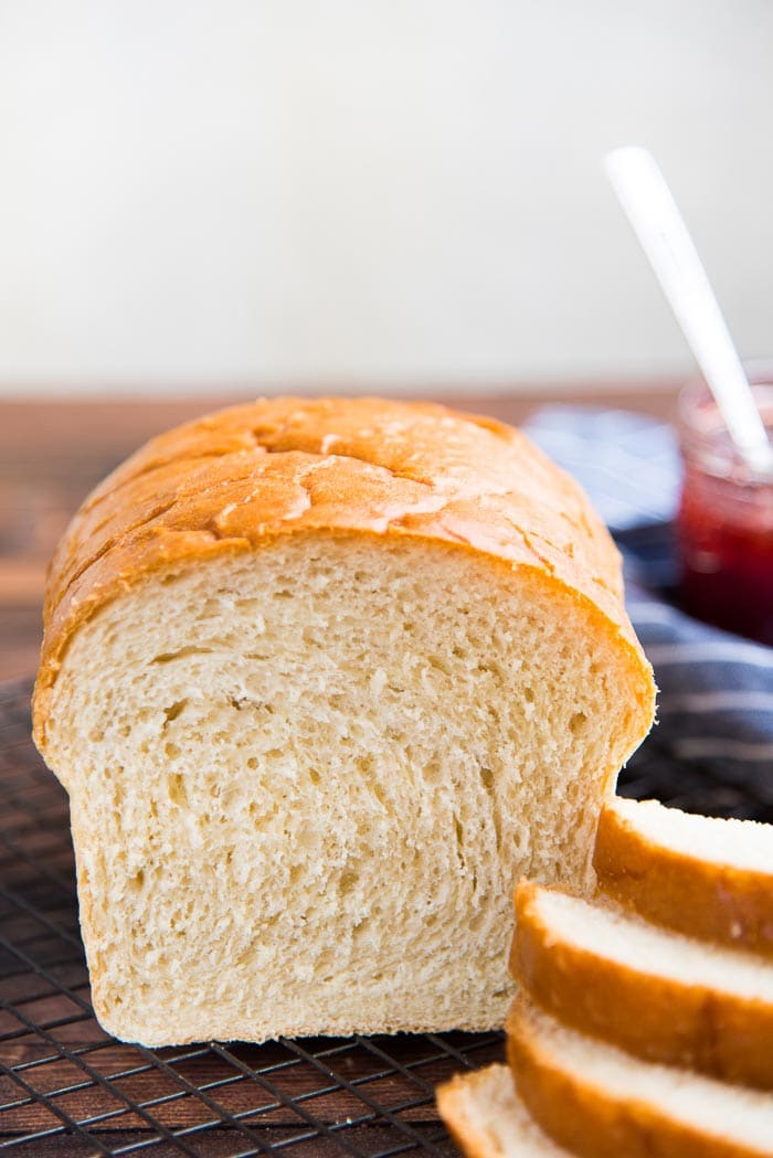A close up of the baked homemade white bread, showing the crumb, next to a stack of sliced bread.