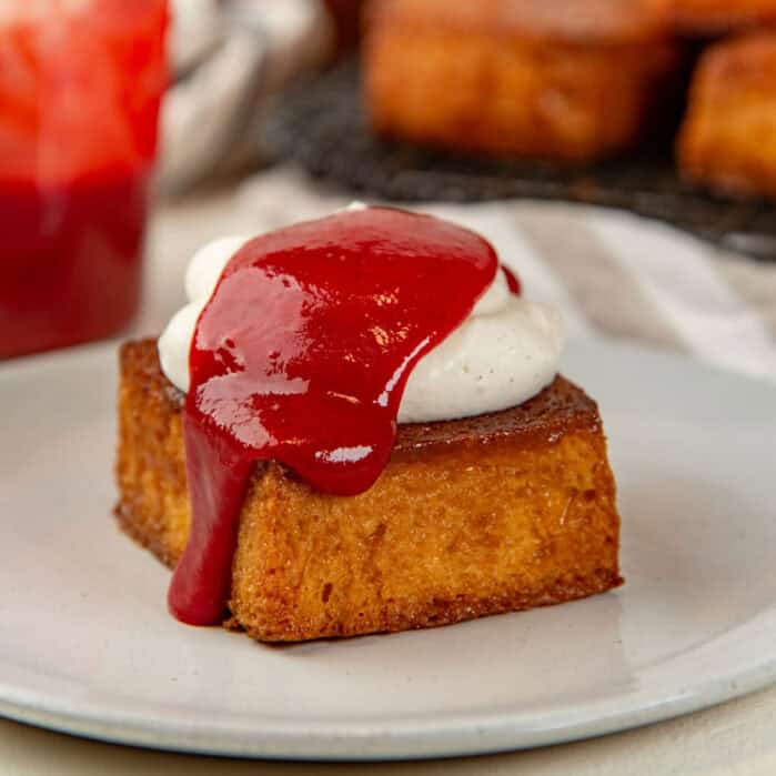 A close up of honey butter toast served with whipped cream and berry coulis.