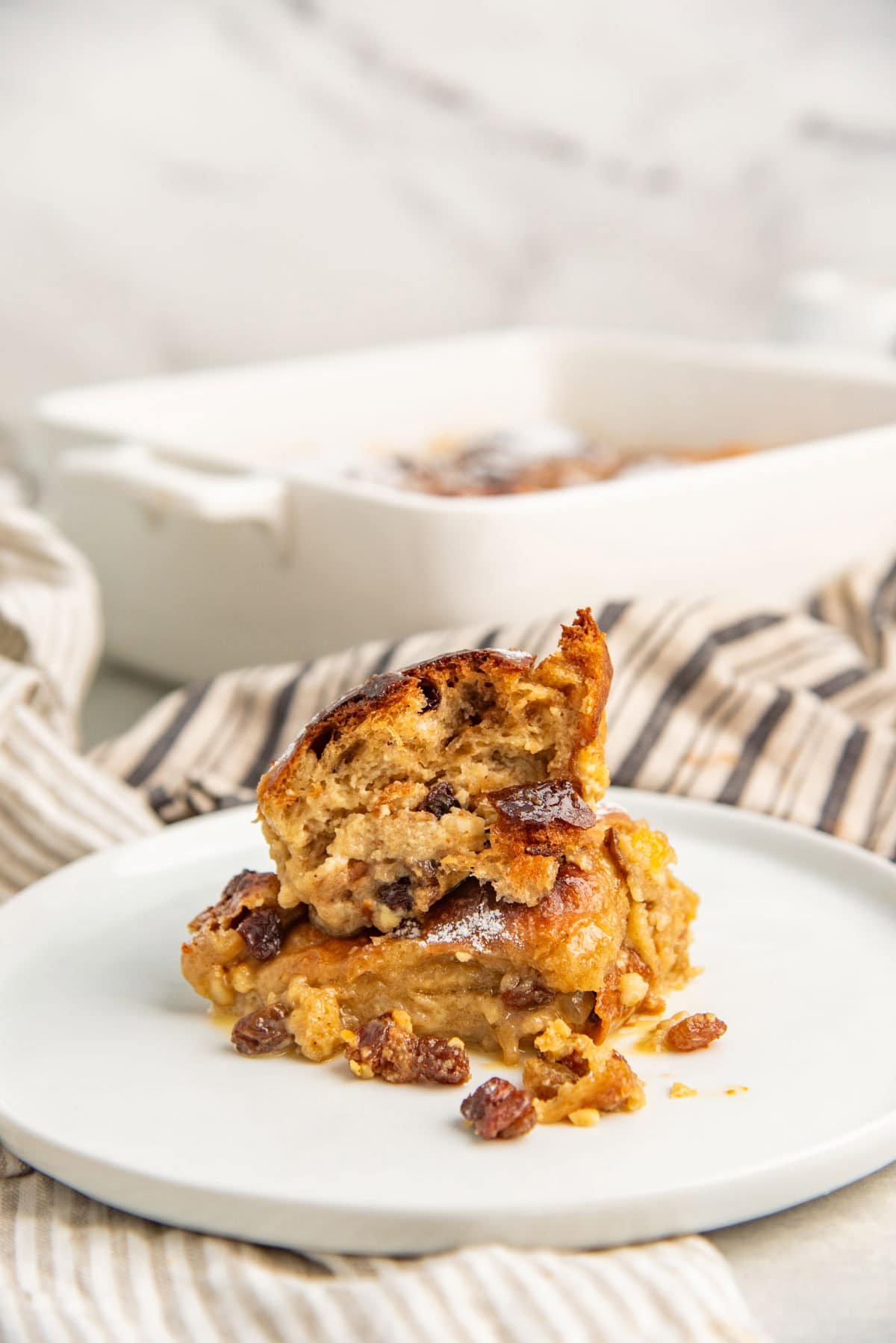 Piece taken out of a serving of the bread pudding to show soft, rich texture and raisins and other add-ins in it.