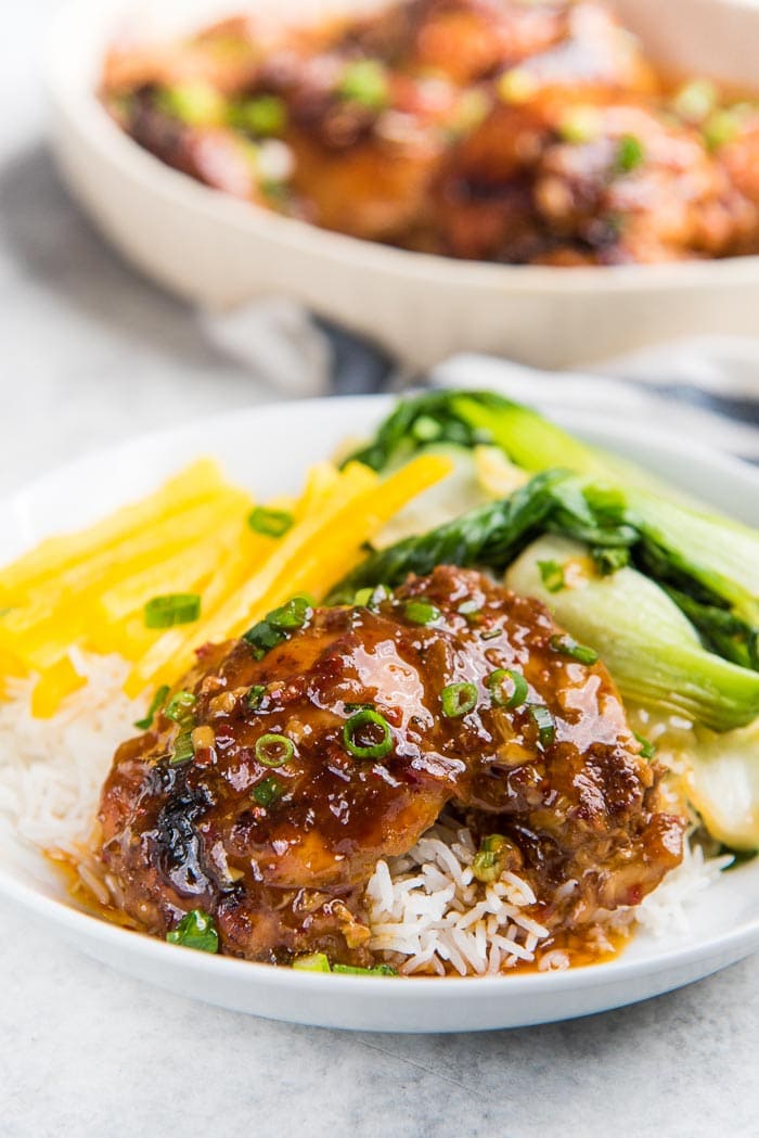 Instant pot chicken thighs with honey soy sauce served ontop of rice with stir fried asian greens and fresh bell peppers, in a white bowl.