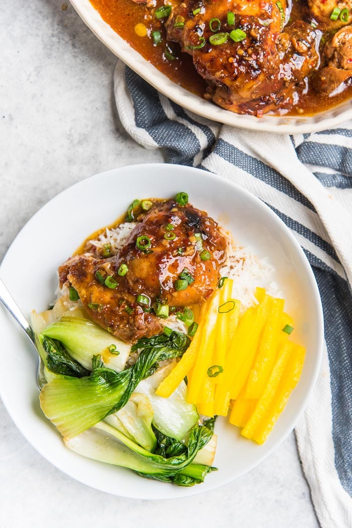 An overhead view of the honey soy chicken thighs served in a white bowl, on top of white rice with stir fried vegetables and cut yellow peppers.