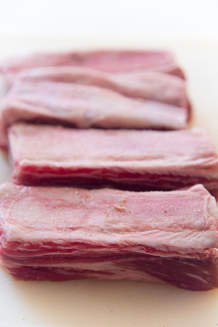Rinsed and dried Beef Short ribs, seasoned with salt on a white cutting board. 