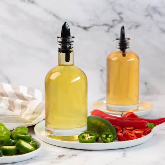 Square image of jalapeno simple syrup and red chili simple syrup in two separate bottles.