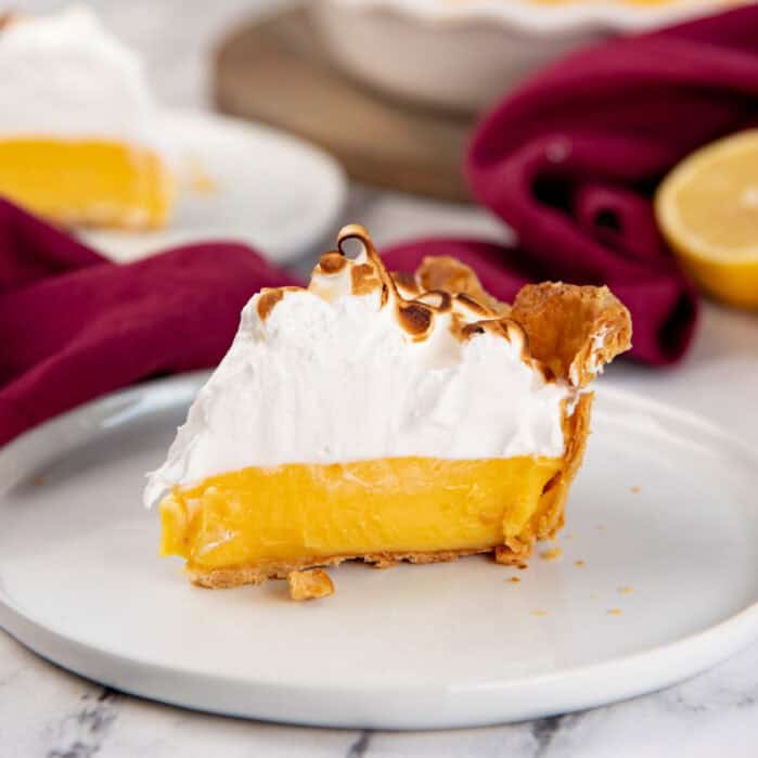 Lemon meringue pie slice on a white plate.