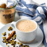 Masala chai in a mug with whole spices used to make the spice mix next to it.