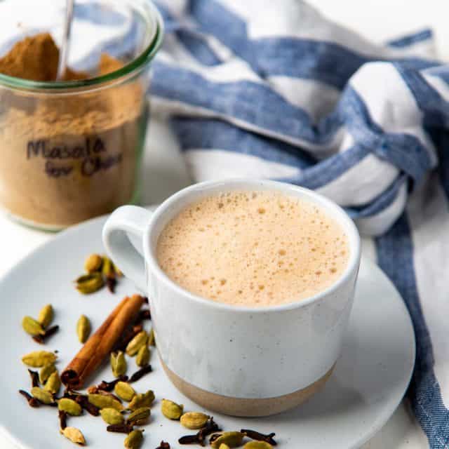 Masala chai in a mug with whole spices used to make the spice mix next to it.