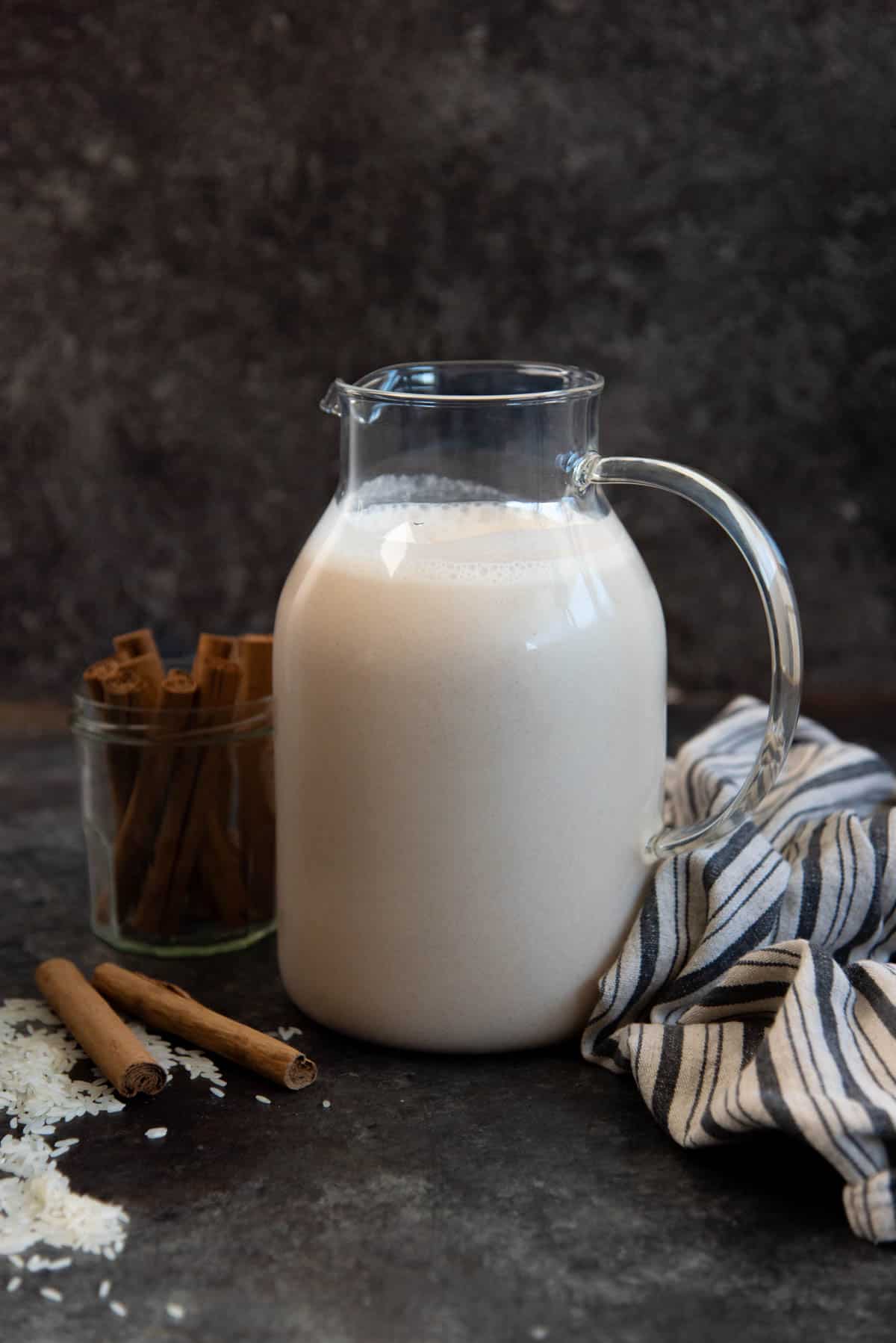 Chilled rice horchata in a big serving jug with cinnamon sticks on the side.