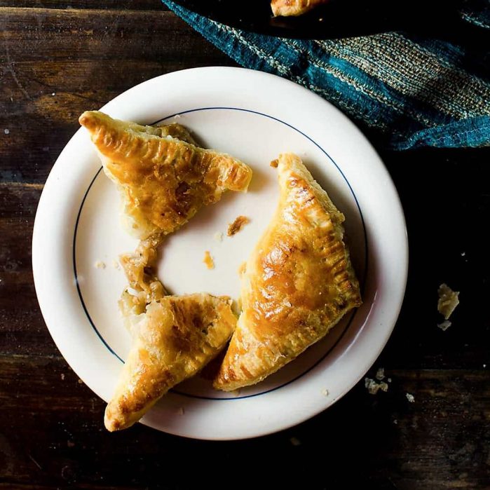 Two puff pastry French onion pies on a white plate, with one broken in half to show the onion filling.