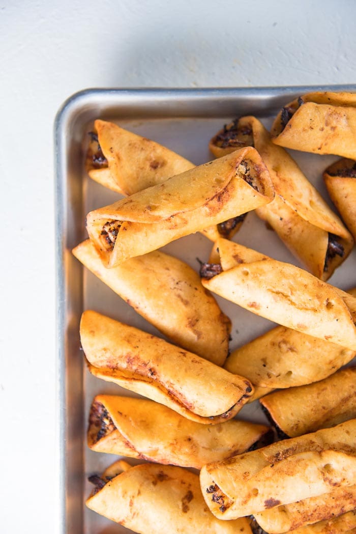 An overhead view of fried mini chicken taquitos on a baking tray.