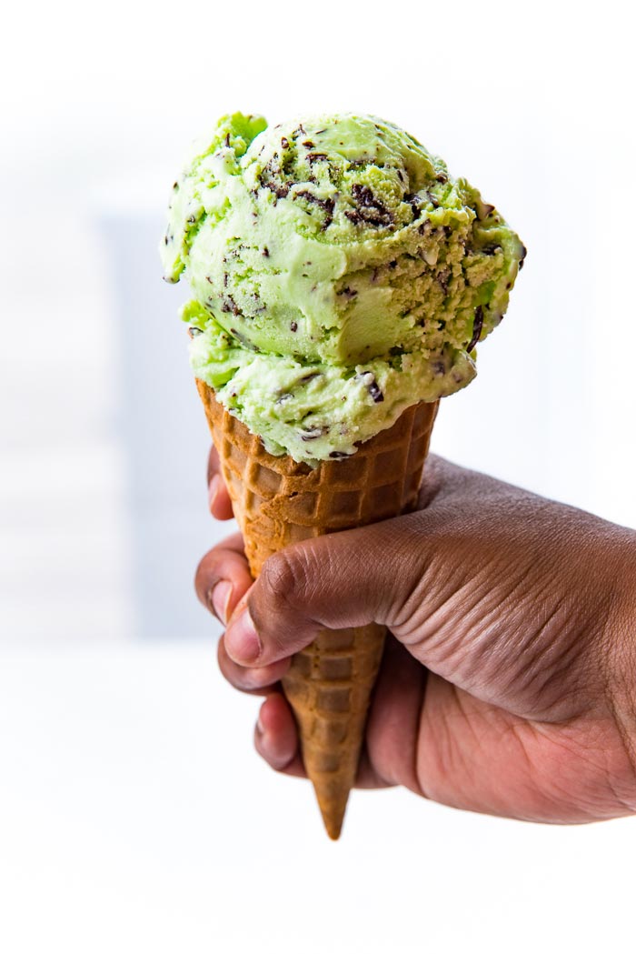 Mint Chocolate Chip Ice cream scooped on top of a waffle cone help up by a hand. 