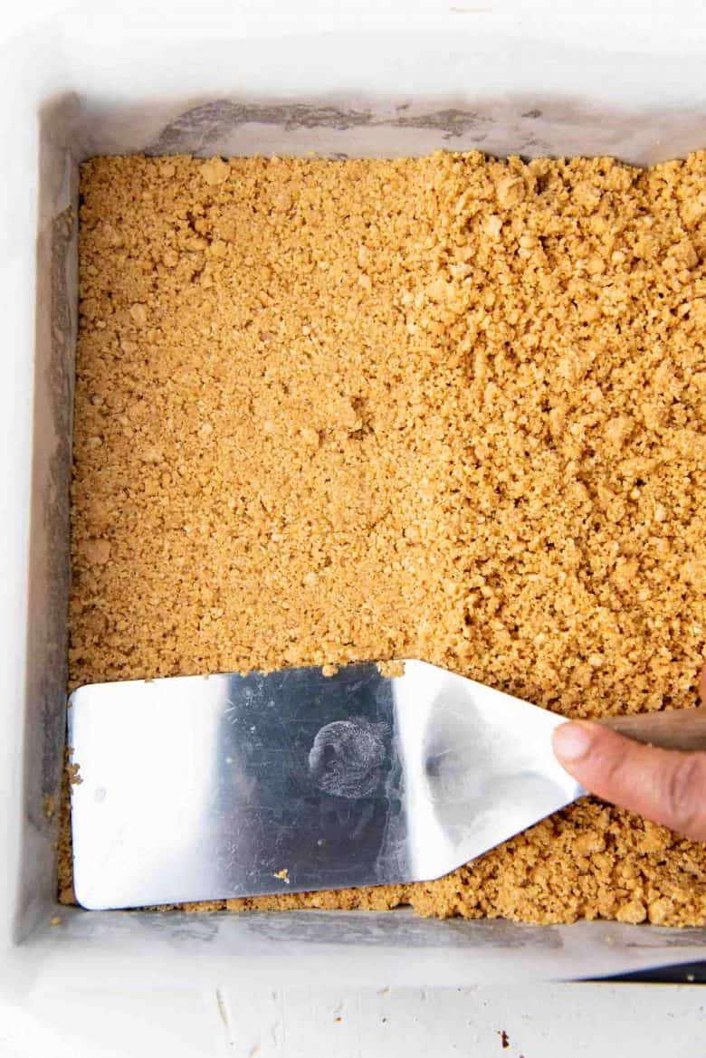 Cracker crumbs being pressed into the bottom of the prepared pan