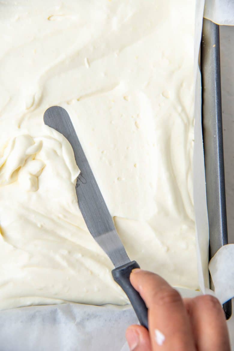 The lemon cheesecake mixture being spread in the prepared pan ontop of the crust