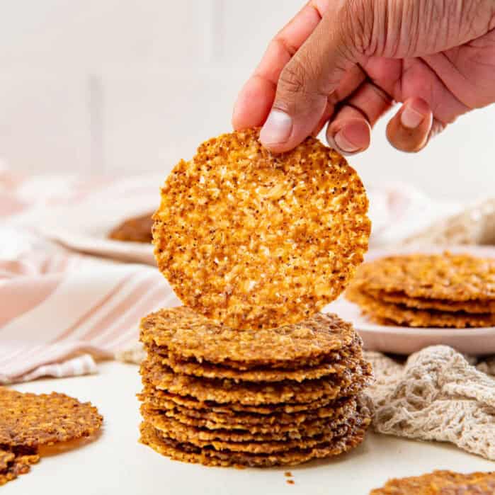 Stack of oatmeal lace cookies, with a hand picking up the cookie on top.