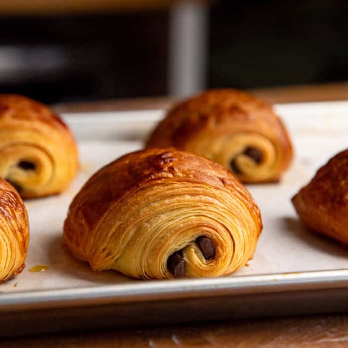 Baked chocolate croissants on a baking sheet showing all the flaky layers and golden brown surface.