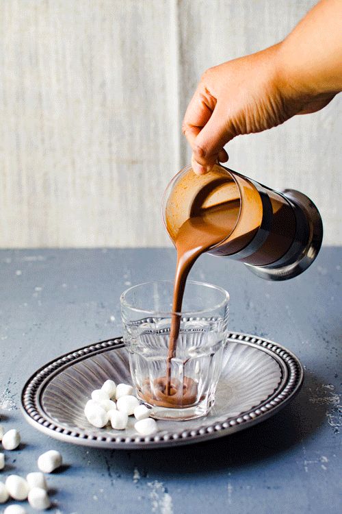 A GIF of thick hot chocolate being poured into a glass from a jug and served with some mini marshmallows.