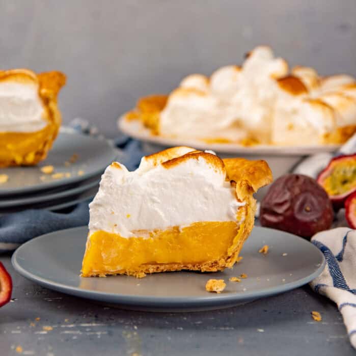 Slice of passion fruit meringue pie on a plate with the rest of the pie in the background.