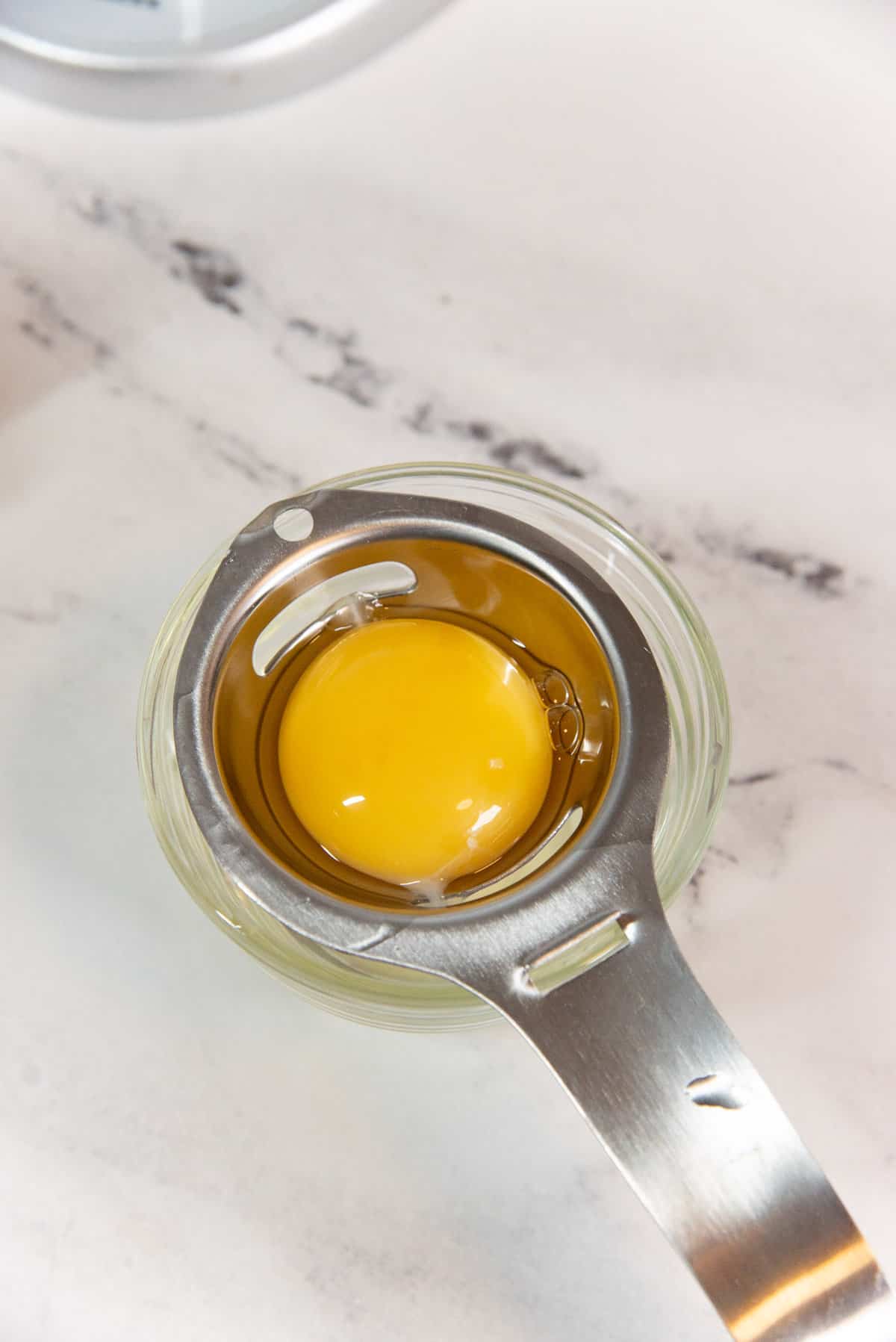 An egg yolk inside an egg separator, with the egg whites strained underneath into the smaller bowl.