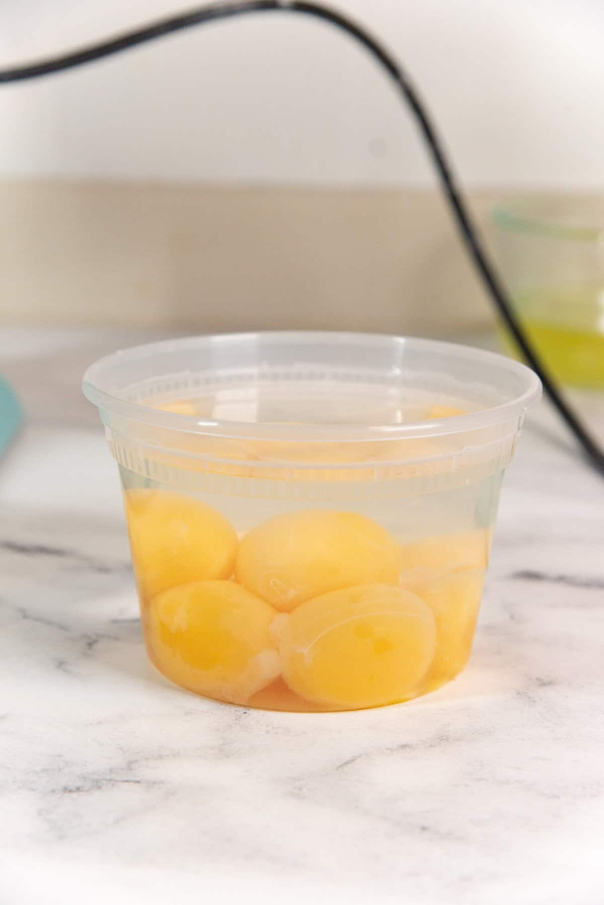 A side view of egg yolks placed in a deli cup with water covering the egg yolks, as a method to store extra egg yolks.