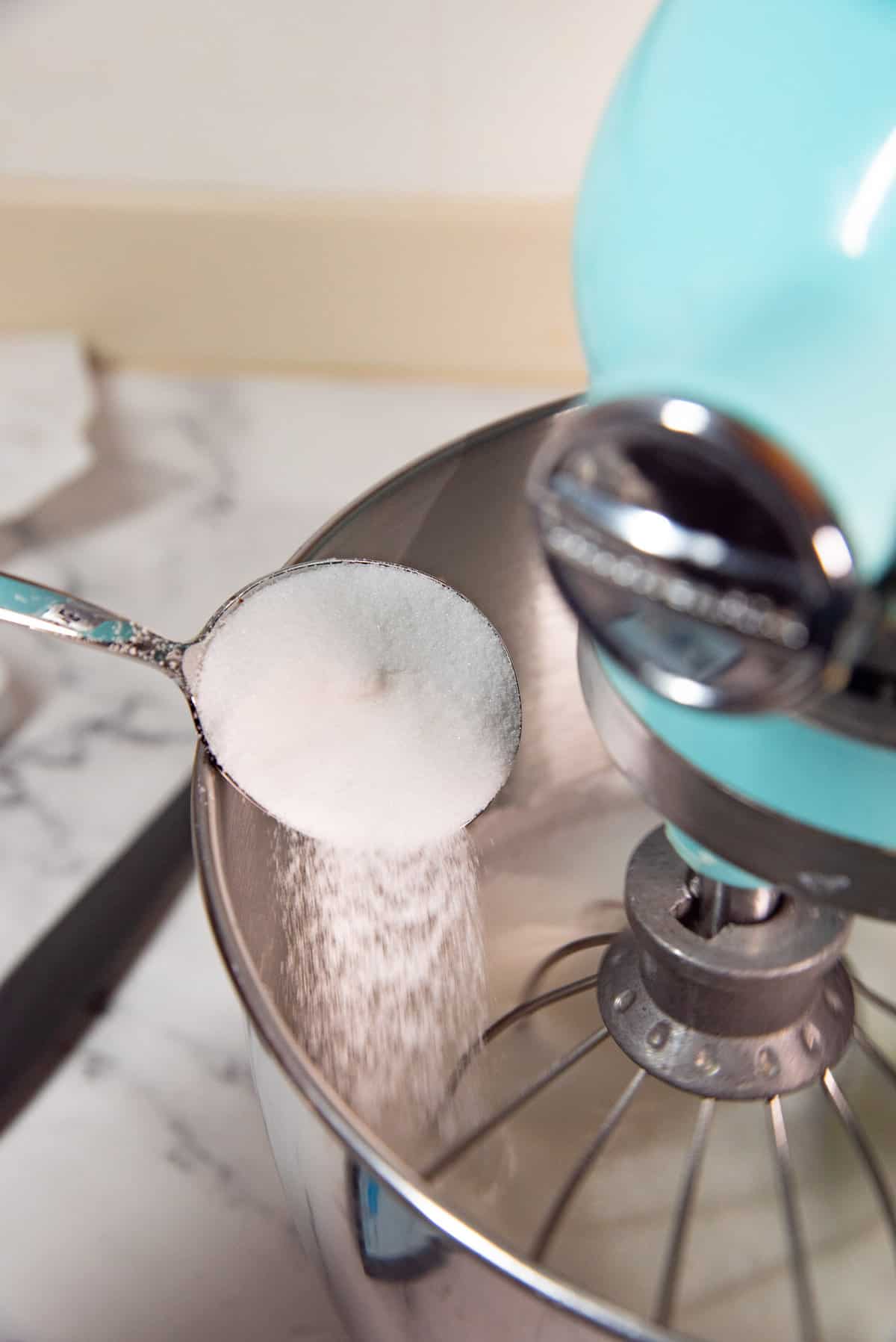 An image of a spoonful of sugar being added slowly into the meringue. 
