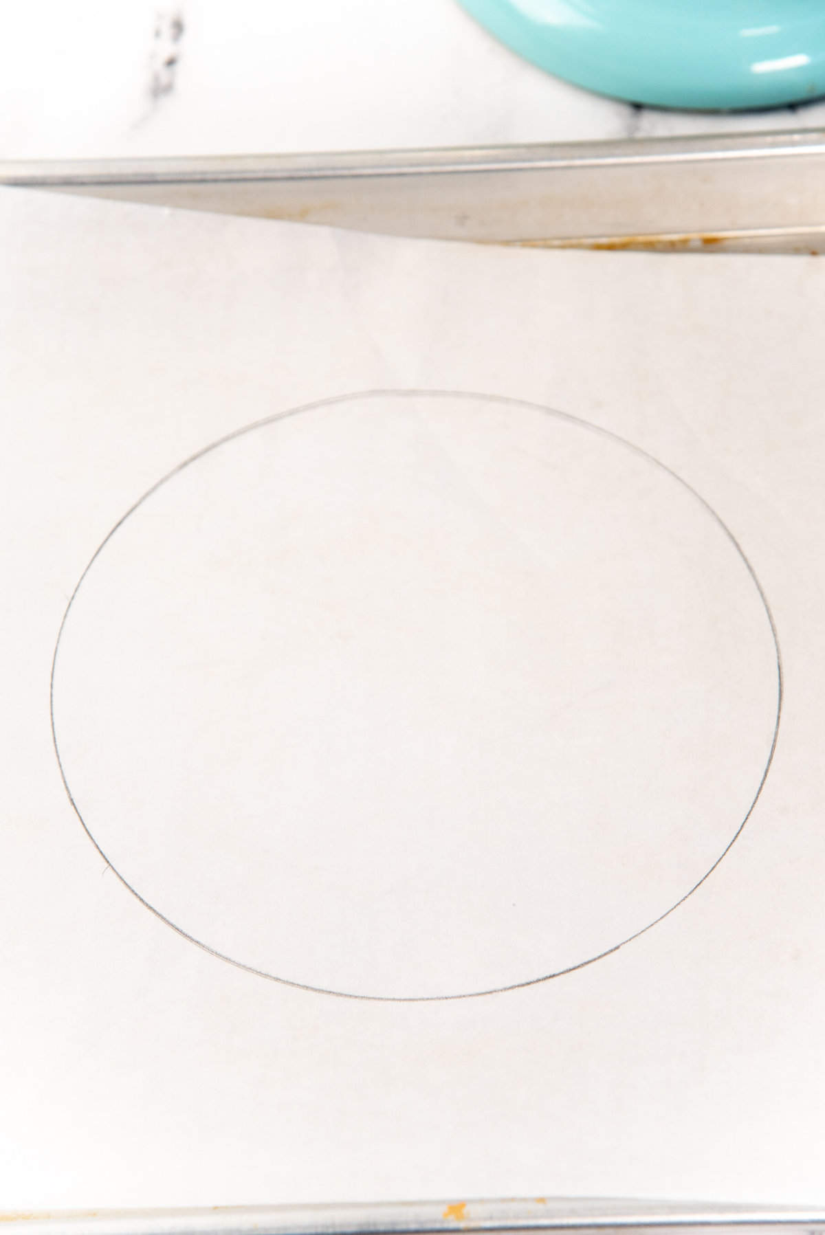 A circle drawn with a pencil on a parchment paper that is placed on a baking tray.