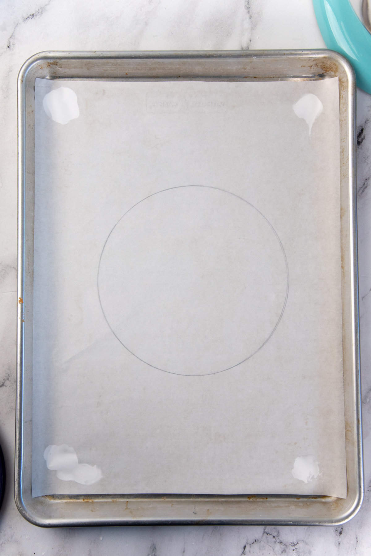 The parchment paper stuck to the baking tray using the meringue dabs, with the drawn circle on the underside.