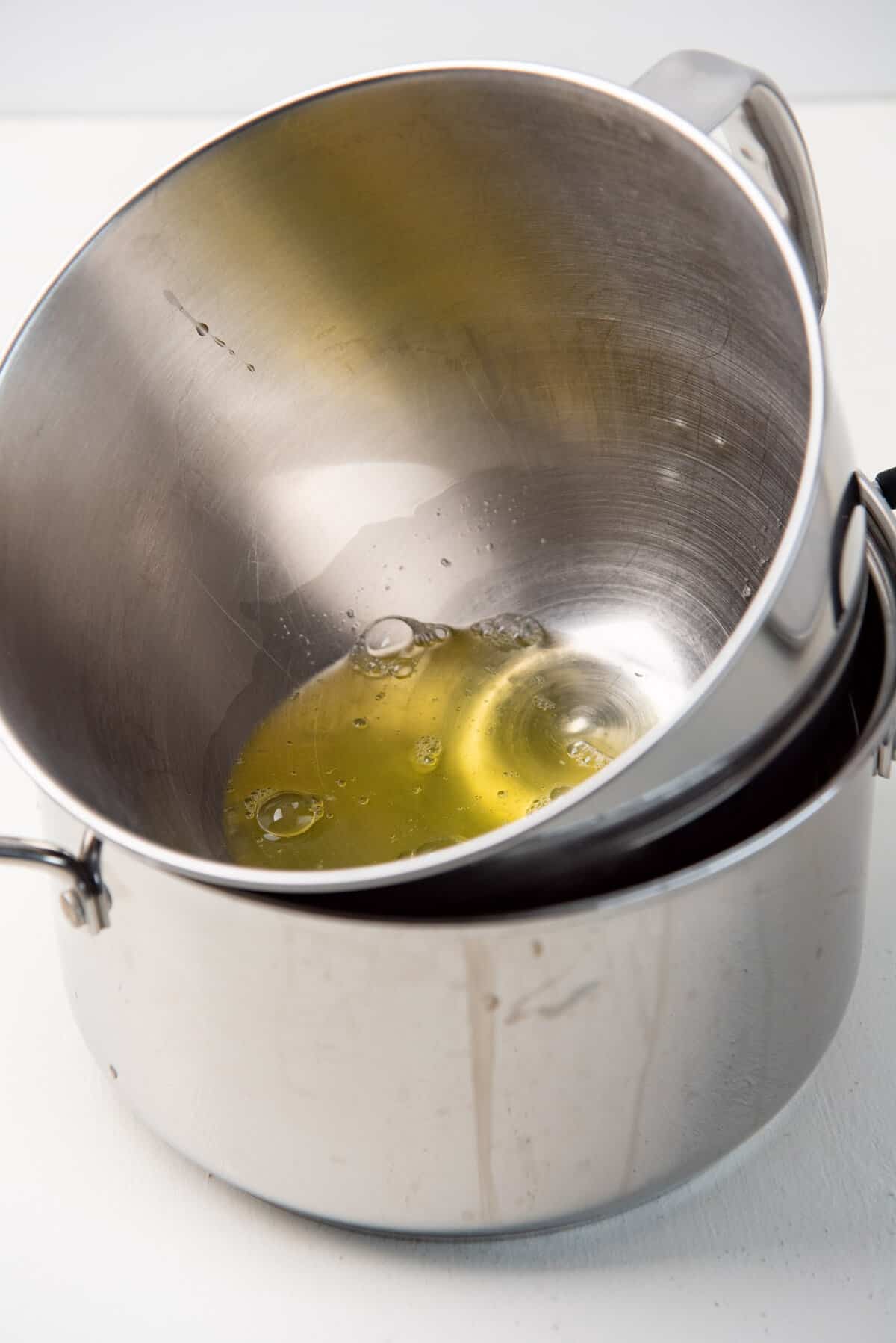 An image of a metal mixing bowl containing egg whites, placed ontop of a large pot that contains hot tap water to gently warm the egg whites.