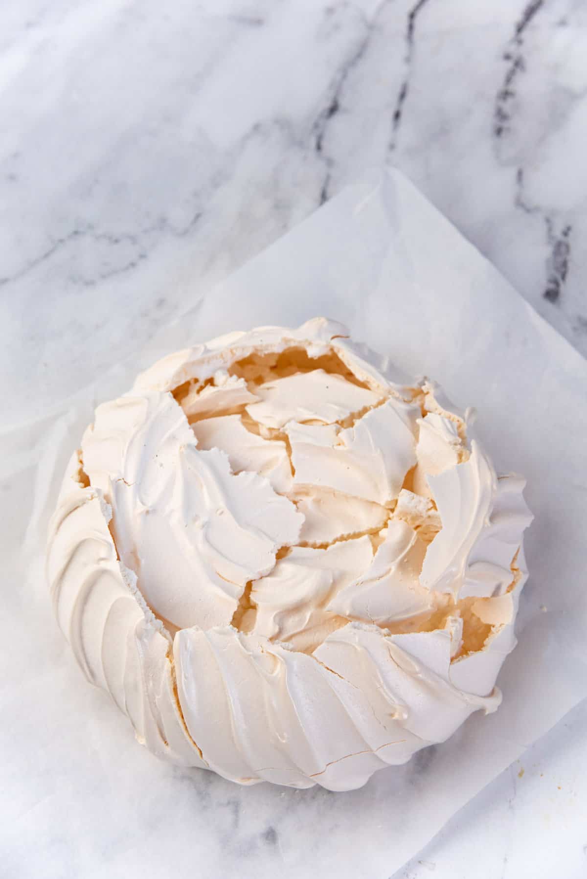 An image of a pavlova, with the top layer carefully cracked so that it lays on top of the marshmallow center inside, to prevent the pavlova collapsing with whipped cream.